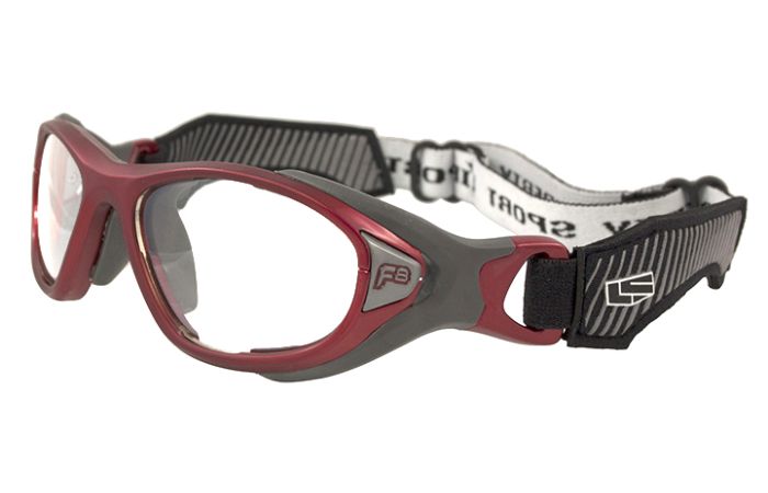A pair of RecSpecs Helmet Spex sports goggles with a red and gray frame. The goggles feature clear lenses and an adjustable black-and-white strap with a buckle for secure fitting, meeting impact resistance standards. Black padded sections on the sides enhance comfort during use.